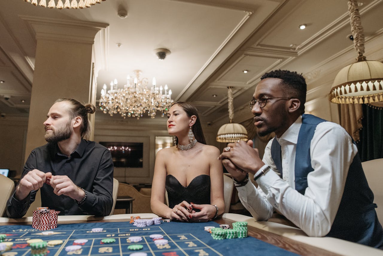 Three players engaged in a game at a casino table under elegant chandeliers, showcasing a luxurious atmosphere.